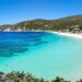 Crystal blue waters lapping against a sun-drenched Greek island beach.