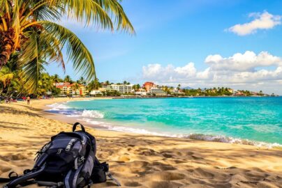 Sunny beach with backpack and colorful coastal buildings.