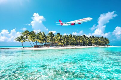 Tropical beach with Virgin Atlantic airplane in blue sky.
