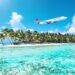 Tropical beach with Virgin Atlantic airplane in blue sky.