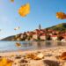 Autumn beach scene with village and golden leaves.