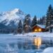 Snowy mountains, cabin, and frozen lake in winter.